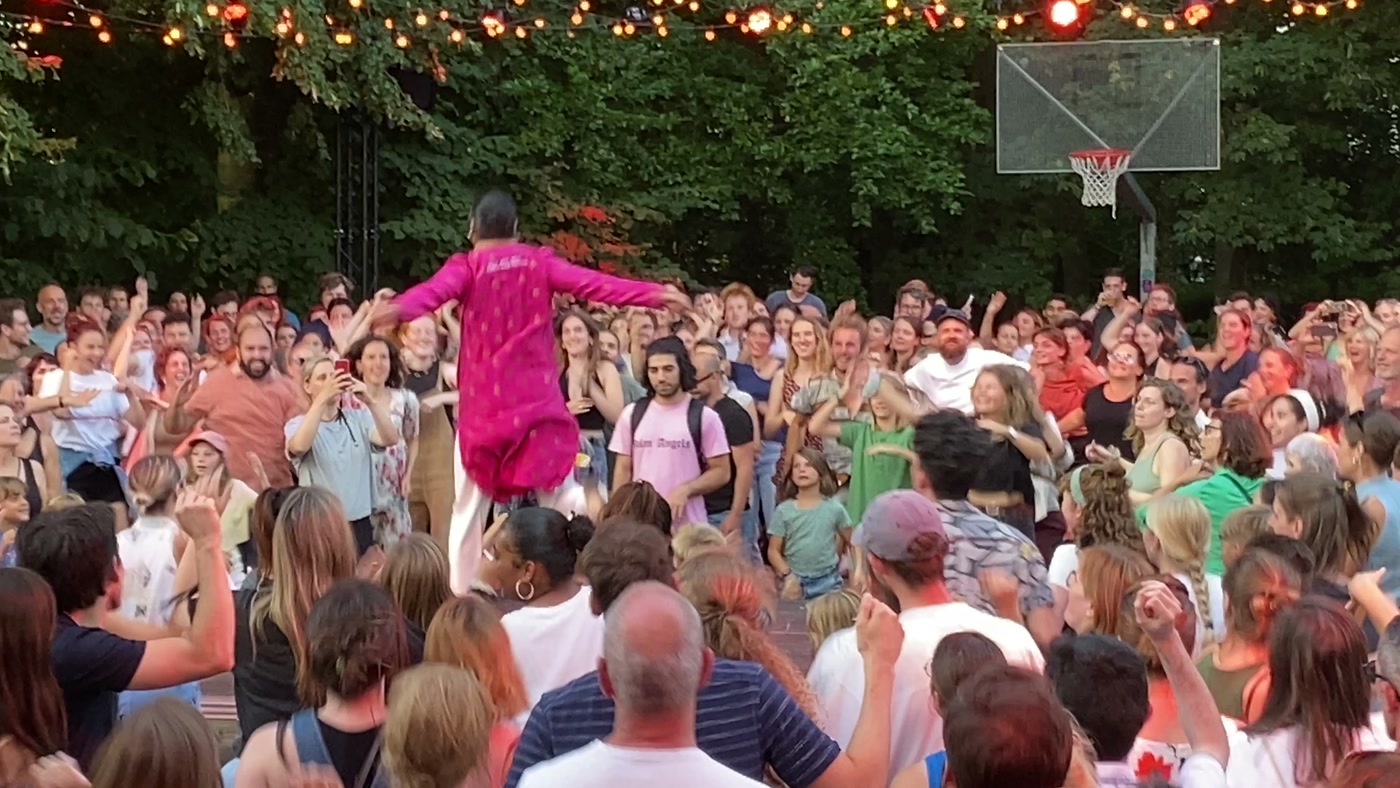 Swapnil raised above a large outdoor crowd, arms wide, hundreds of people dancing with him